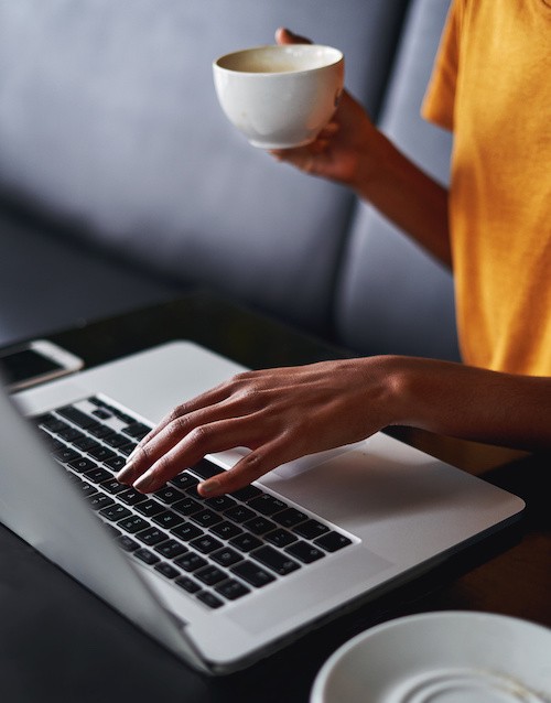 Women typing on laptop holding coffee cup